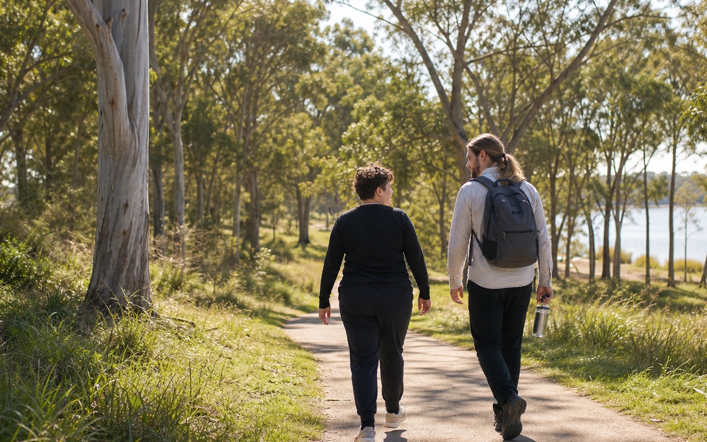 Participant and support worker walking side by side on a sunny lakeside path