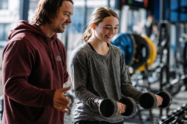 Support worker guiding a participant through dumbbell exercises in a gym